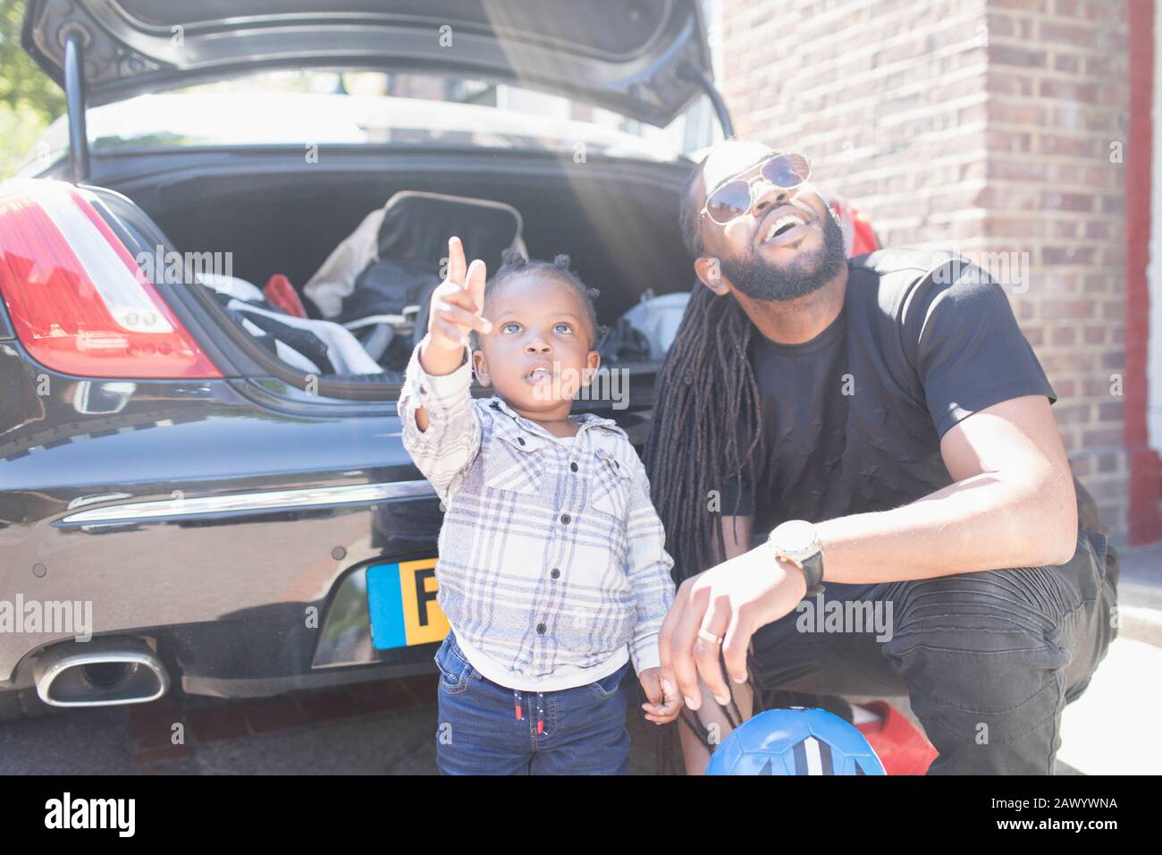 Vater und neugieriger Kleinkind, der hinter dem Auto aufblickt Stockfoto