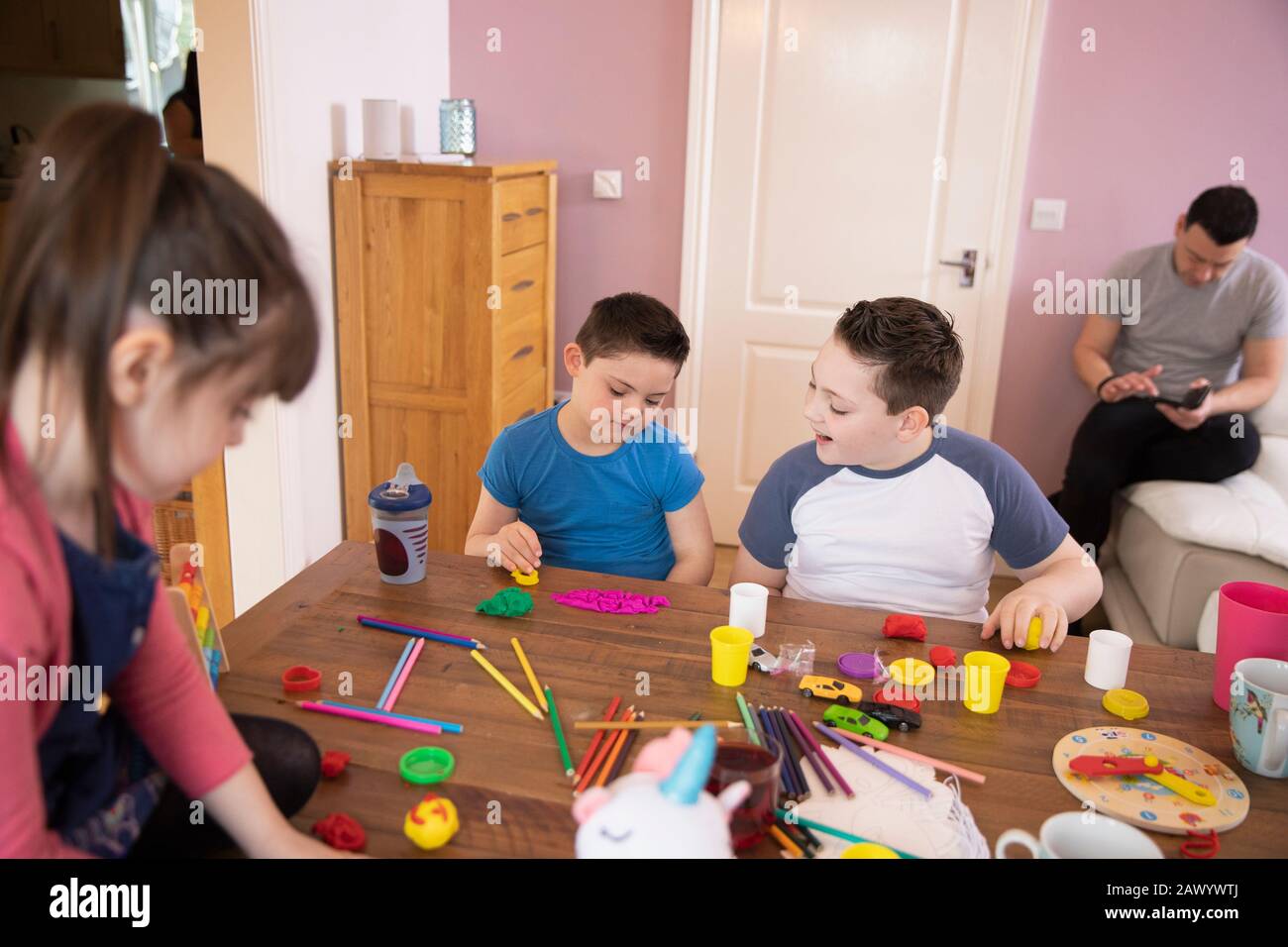 Junge mit Down-Syndrom und Geschwistern, die mit Spielzeug am Tisch spielen Stockfoto