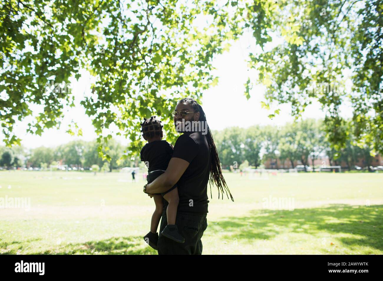 Portrait glücklicher Vater mit langen Zitzen, die Sohn im sonnigen Park tragen Stockfoto