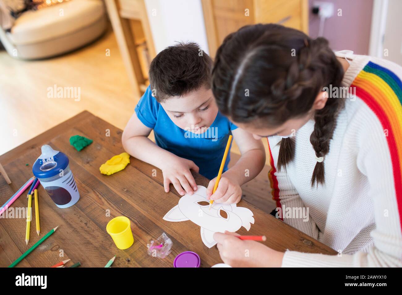 Mädchen, die Bruder mit Der Farbe Des Down-Syndroms am Tisch helfen Stockfoto