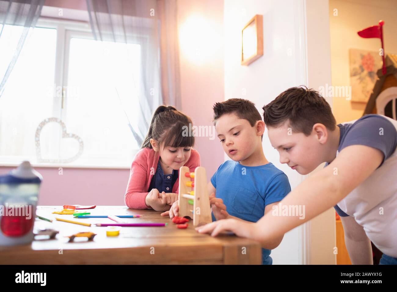 Junge mit Down-Syndrom und Geschwistern, die mit Spielzeug am Tisch spielen Stockfoto