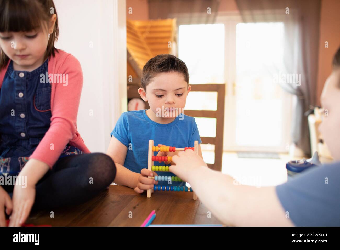 Junge mit Down-Syndrom und Geschwistern, die mit Spielzeug am Tisch spielen Stockfoto