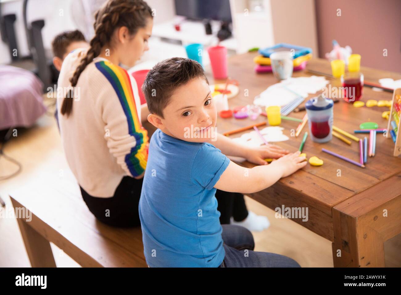 Portrait niedlicher Junge mit Daung-Syndrom-Farbgebung am Tisch mit Schwester Stockfoto