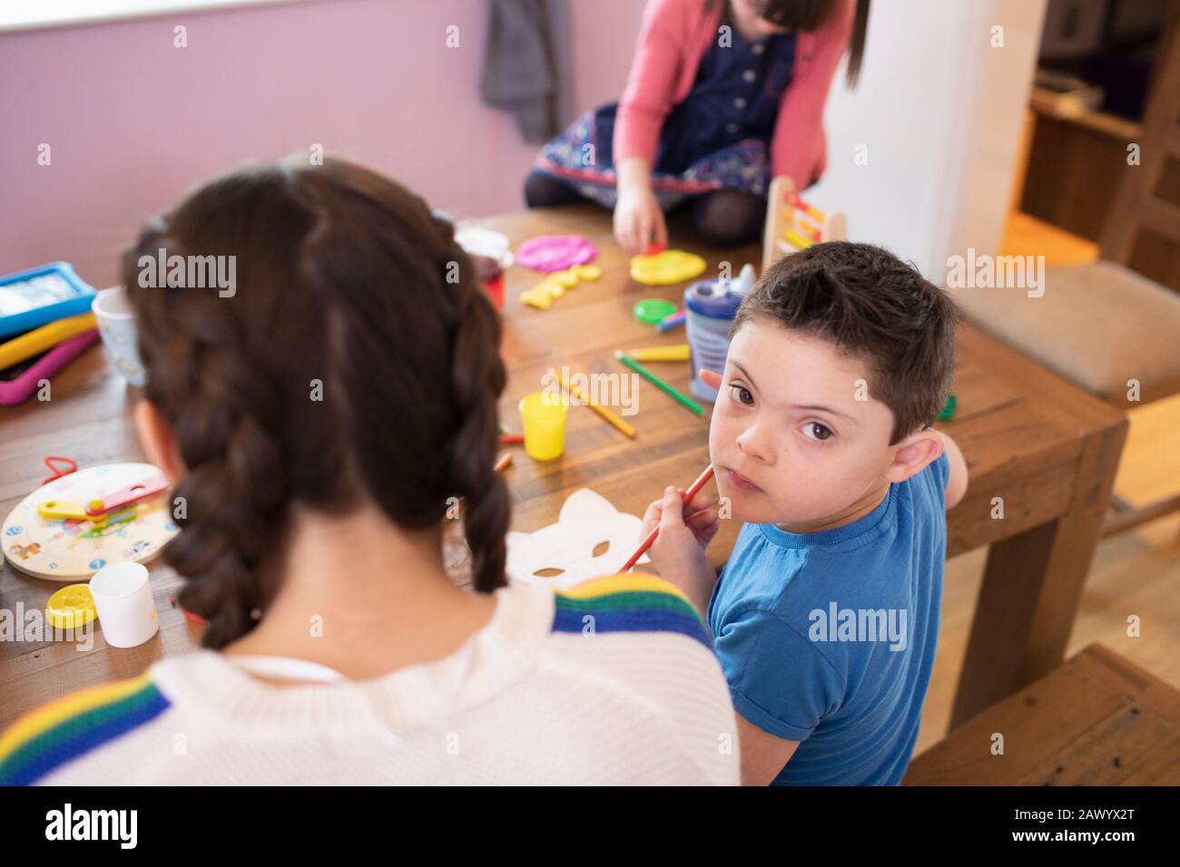 Portrait niedlicher Junge mit Daung-Syndrom-Farbgebung am Tisch mit Geschwistern Stockfoto
