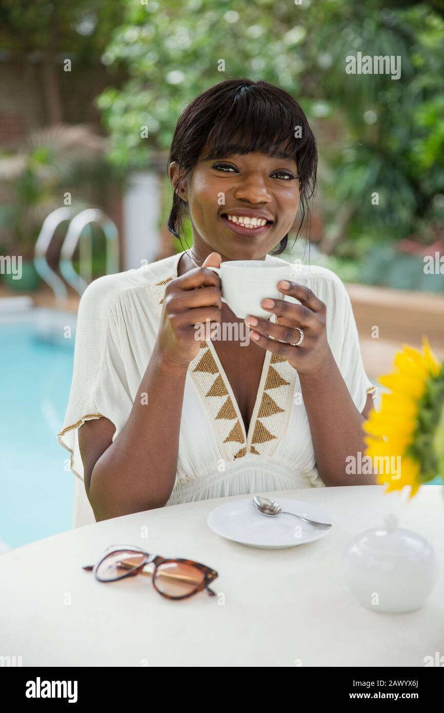 Portrait fröhliche junge Frau trinkt Kaffee am Pool Stockfoto