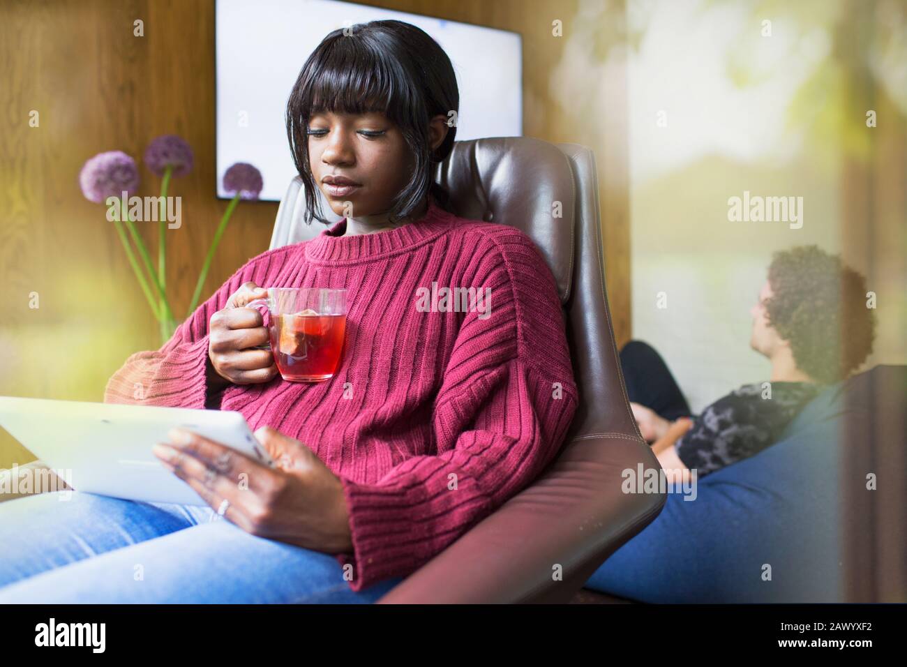 Junge Frau trinkt Tee und verwendet digitale Tablette Stockfoto