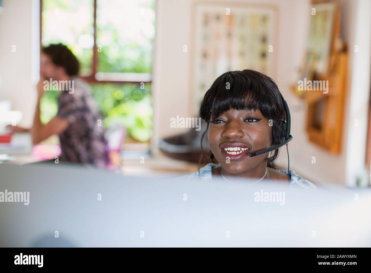 Junge Frau mit Headset, die von zu Hause aus am Computer arbeitet Stockfoto
