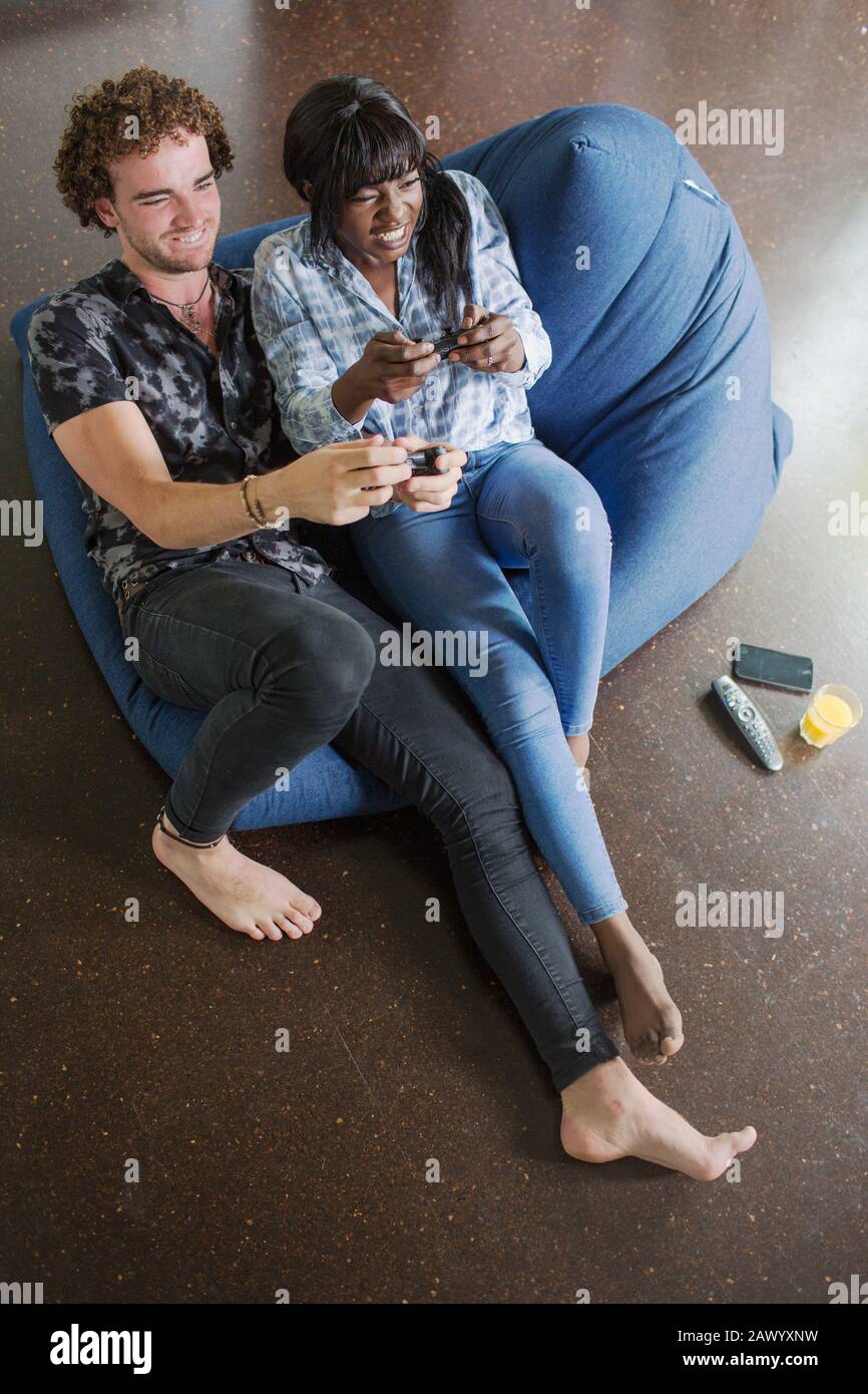 Junges multiethnisches Paar, das Videospiel im Beansack-Stuhl spielt Stockfoto