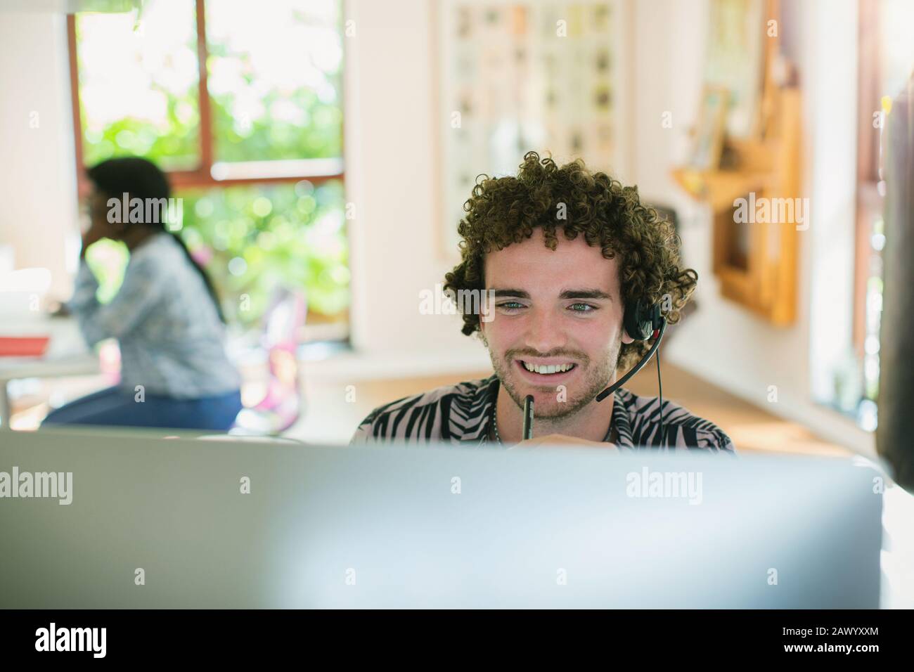 Junger Mann mit Headset, das am Computer im Büro arbeitet Stockfoto