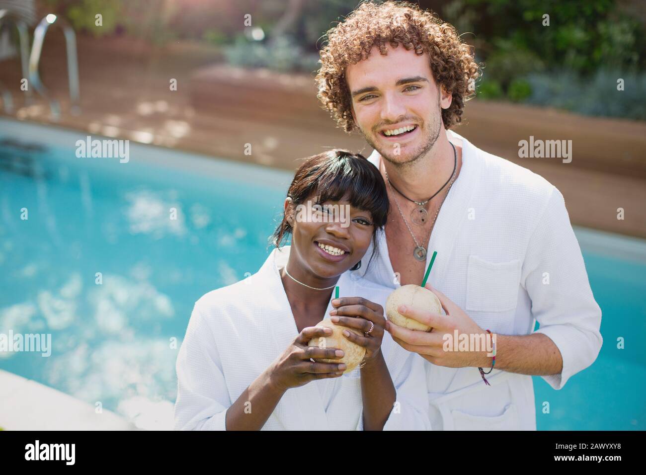 Portrait fröhliches junges Paar in Bademänteln, die am Pool aus Kokosnüssen trinken Stockfoto