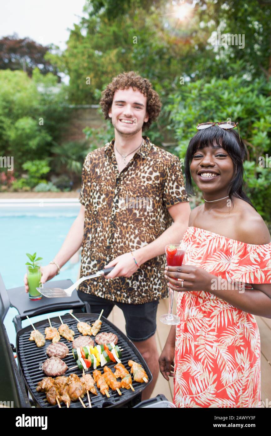 Portrait fröhliches junges multiethnisches Paar, das am Pool grillt Stockfoto