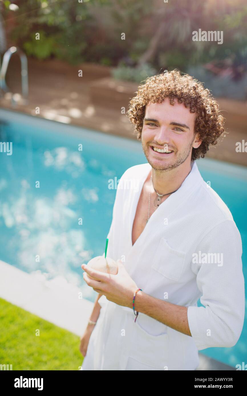 Portrait fröhlicher junger Mann im bademantel, der am Pool aus Kokosnuss trinkt Stockfoto