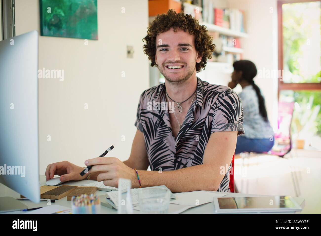 Portrait lächelnder junger Mann, der im Büro am Computer arbeitet Stockfoto