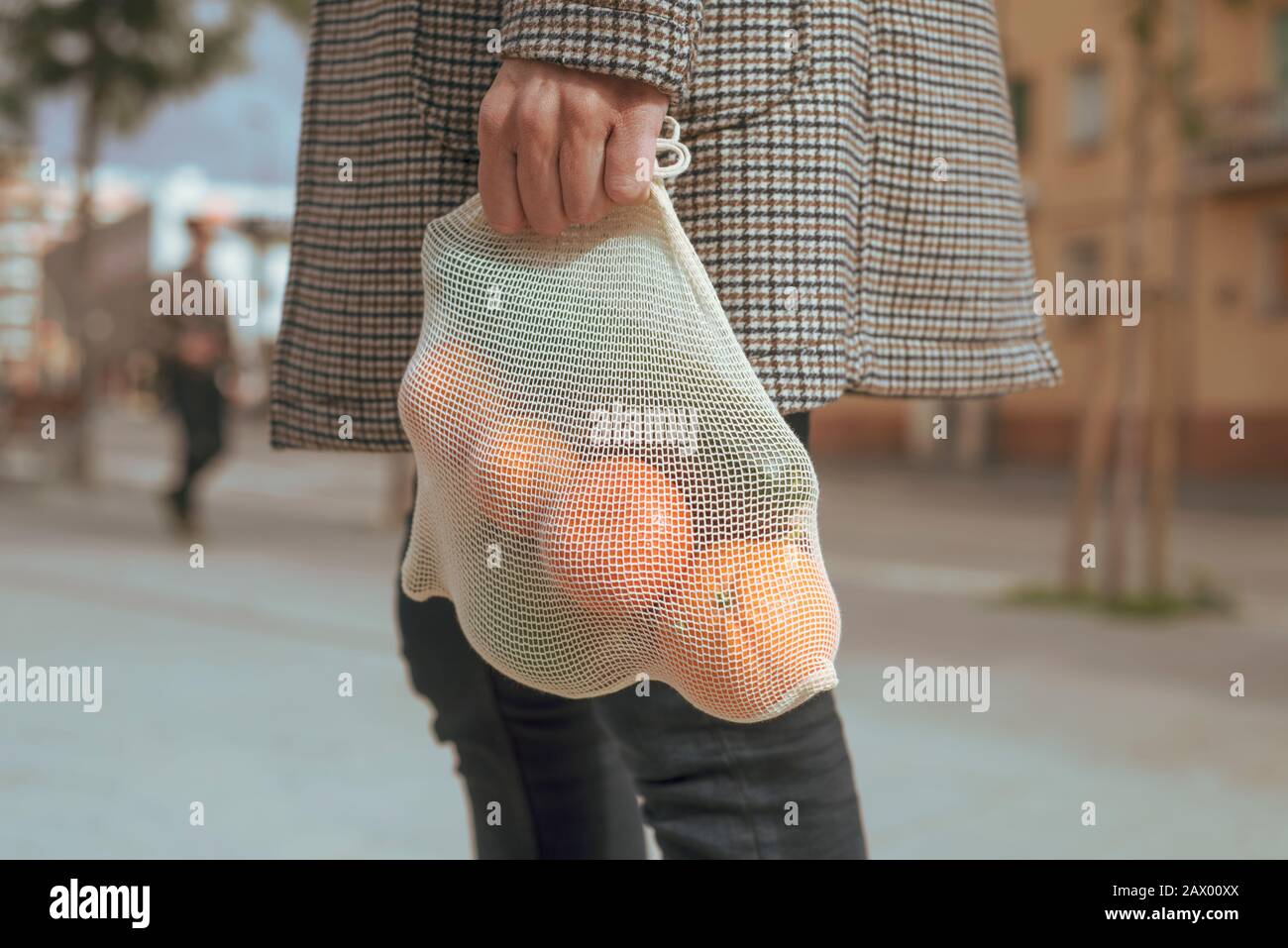 Nahaufnahme eines Mannes auf der Straße, der einen wiederverwendbaren Textil-Netzbeutel trägt, der früher Lebensmittel in großen Mengen, voller Obst und Gemüse, als Maßnahme zum Redu kaufte Stockfoto