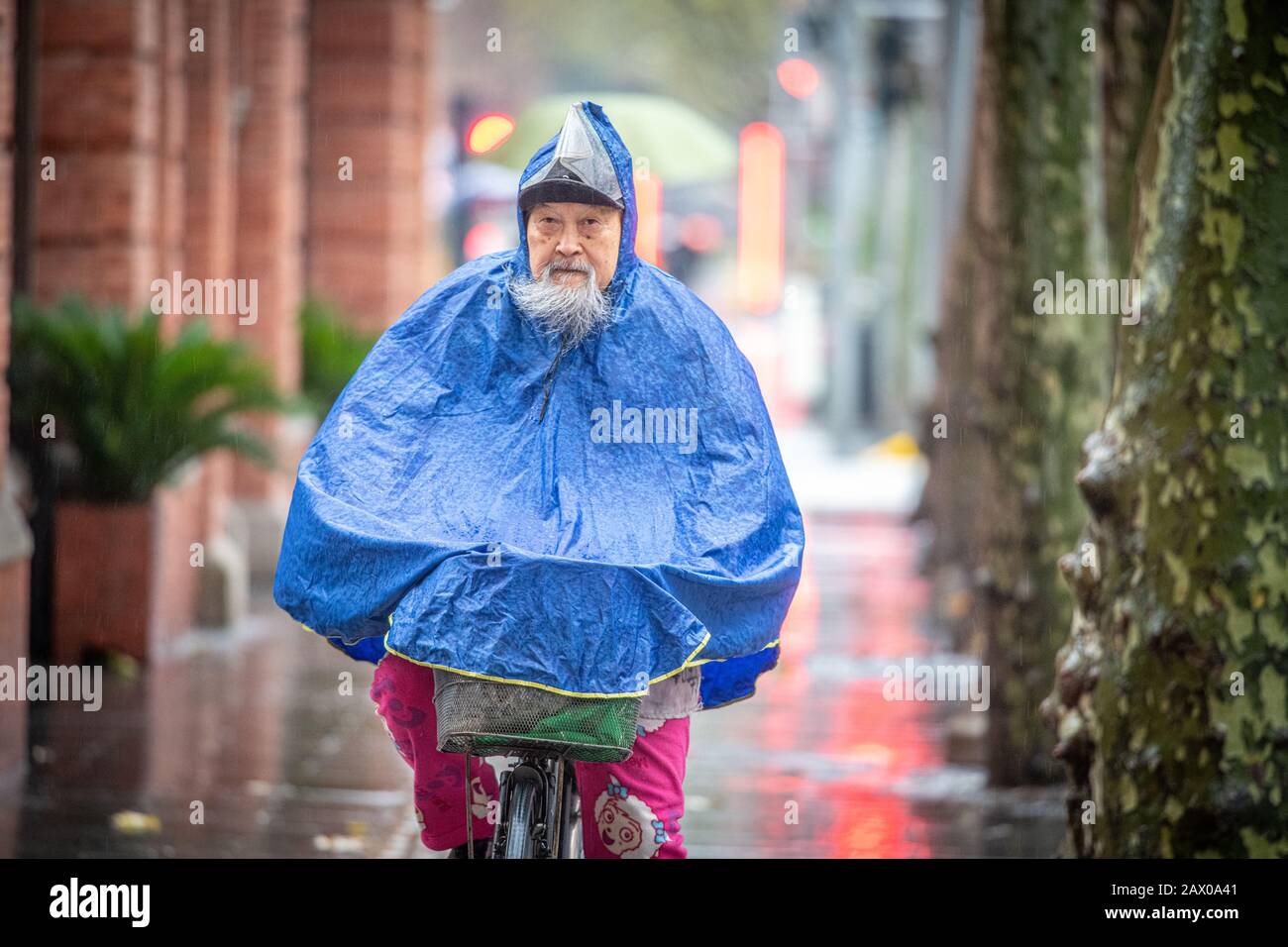 Ein entschlossener älterer Mann fährt mit seinem Fahrrad im Regen, Shanghai, China. Stockfoto