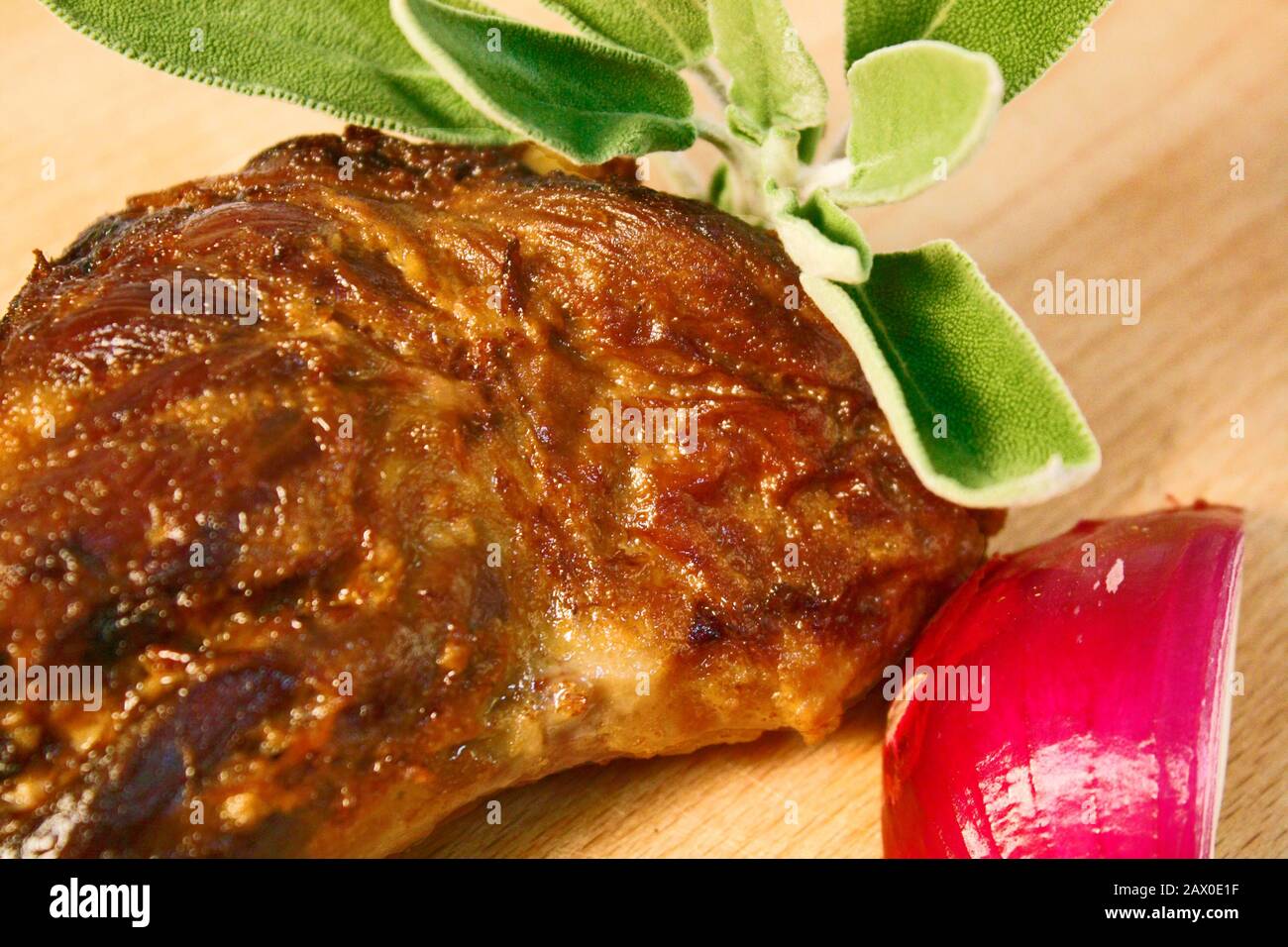 Lammbeinbraten langsam gekocht auf Holzschneidebrett mit roter Zwiebel und frischen Minzblättern. Frühling, Osterabendessen. Stockfoto