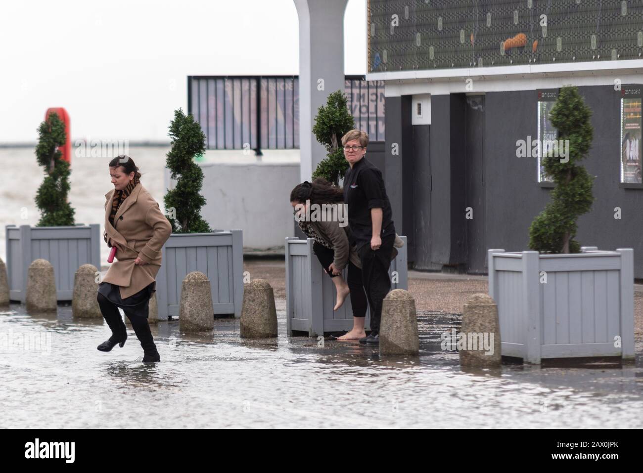 Southend on Sea, Essex, Großbritannien. Februar 2020. Das Ende des Sturms Ciara, kombiniert mit einer Flut, hat die Seeverteidigung entlang der westlichen Esplanade der Stadt durchbrochen und eine Straßensperrung verursacht, nachdem ein Teil des Verkehrs das Wasser gebüßt hat. Betroffen waren Geschäfte an der Meeresfront. Eine Frau wohne durch Flutwasser, während eine andere ihre Schuhe entfernt Stockfoto