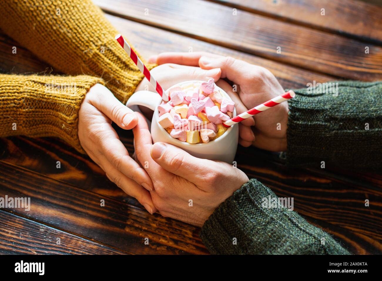 Ein Paar hält die Hände um eine Tasse heißen Schokoladenkakaos mit herzförmigem Marshmallow als Belag Stockfoto