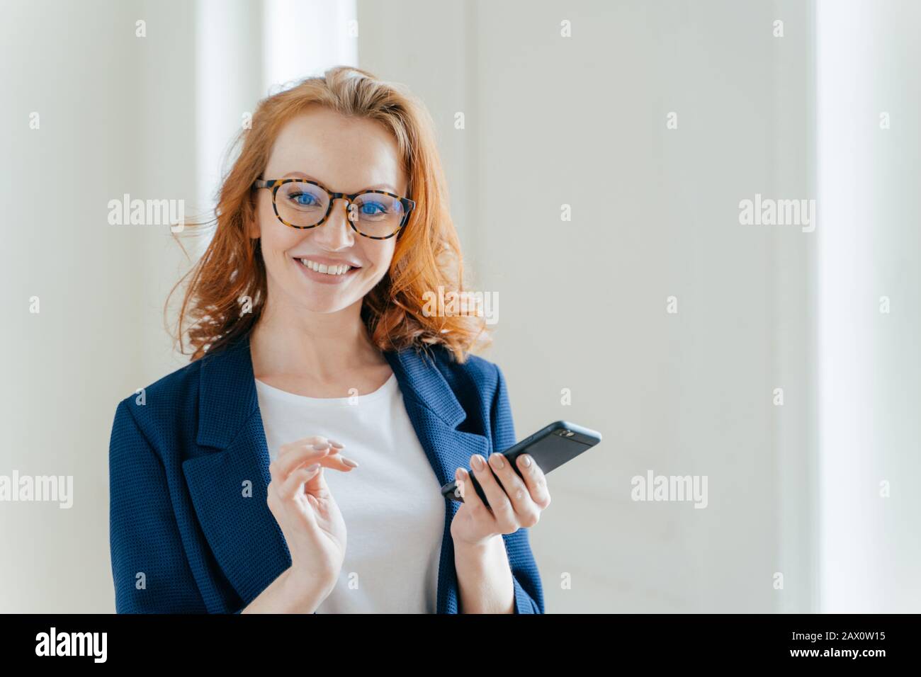 Eleganter Werbetexter mit breitem Lächeln sucht nach Informationen für Artikel und Veröffentlichung auf Handy trägt Brille. Geschäftsfrau lernt detai Stockfoto