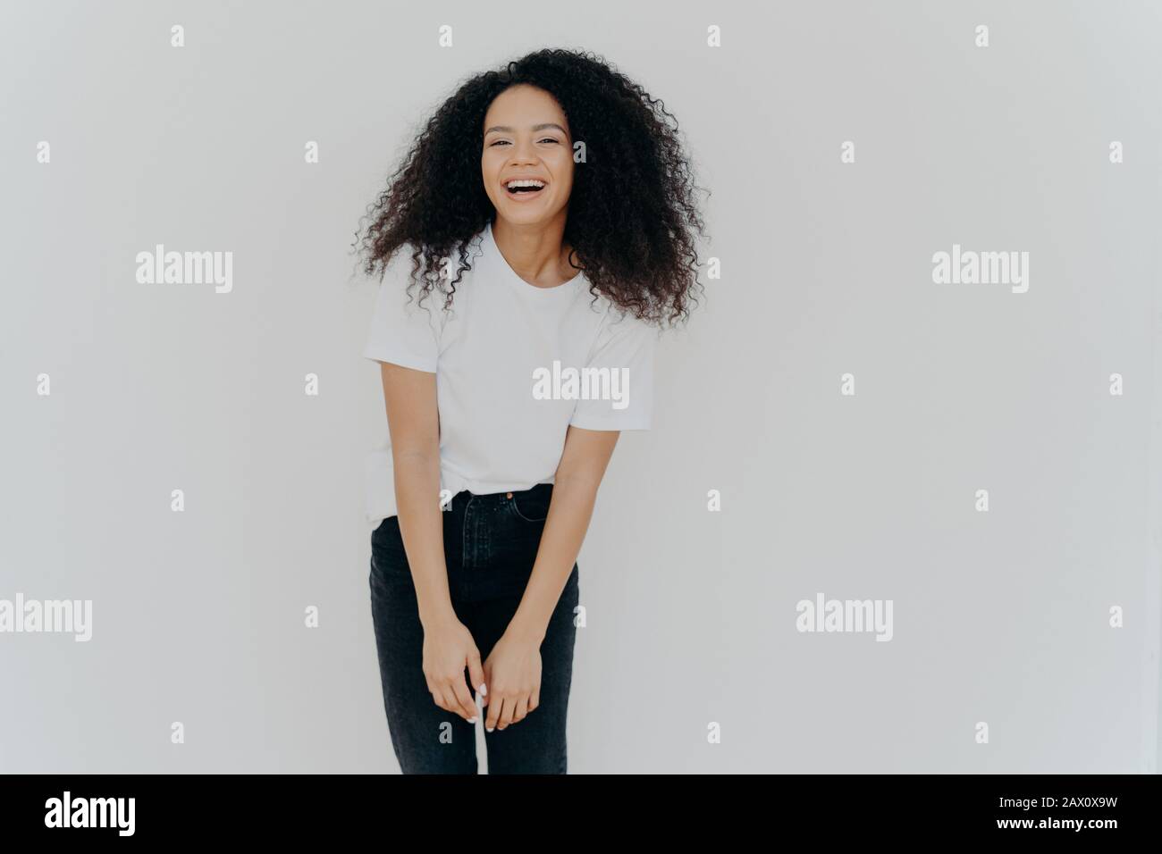 Der Studioschuss der freudigen afroamerikanischen Frau lacht glücklich, gekleidet in legerer Kleidung, fühlt sich gut an, posiert vor weißem Hintergrund mit leerem Raum für y Stockfoto