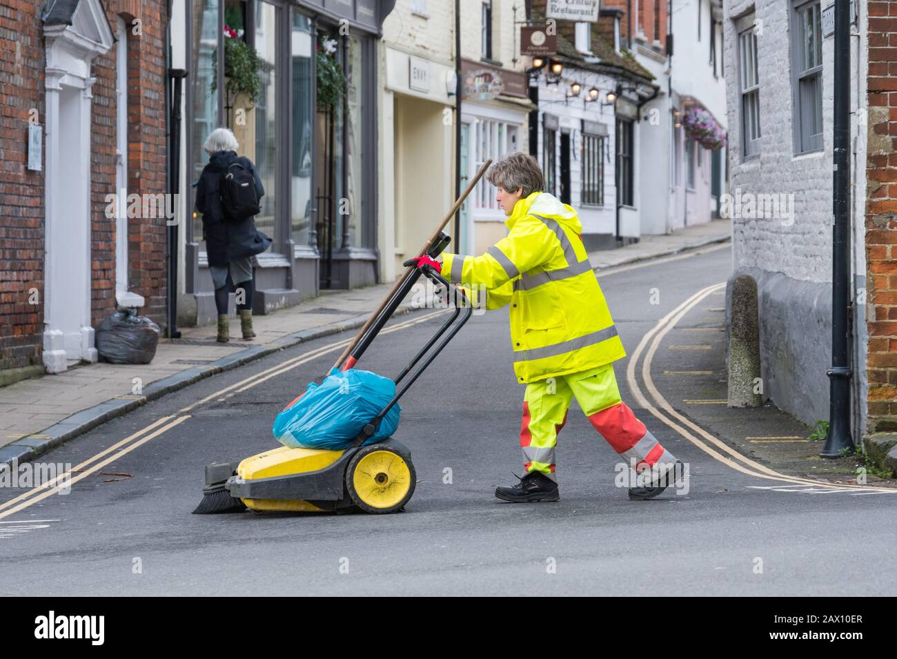 Frau mittleren Alters, die einen Müllwagen drückt, während sie Mülltonnen und Abfälle entfernt, während sie eine Straße in Großbritannien putzt. Weibliche Straßenreinigung. Stockfoto