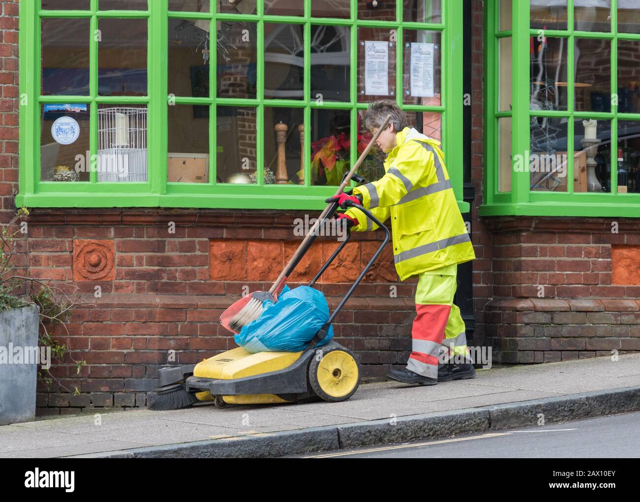 Frau mittleren Alters, die einen Müllwagen drückt, während sie Mülltonnen und Abfälle entfernt, während sie eine Straße in Großbritannien putzt. Weibliche Straßenreinigung. Stockfoto