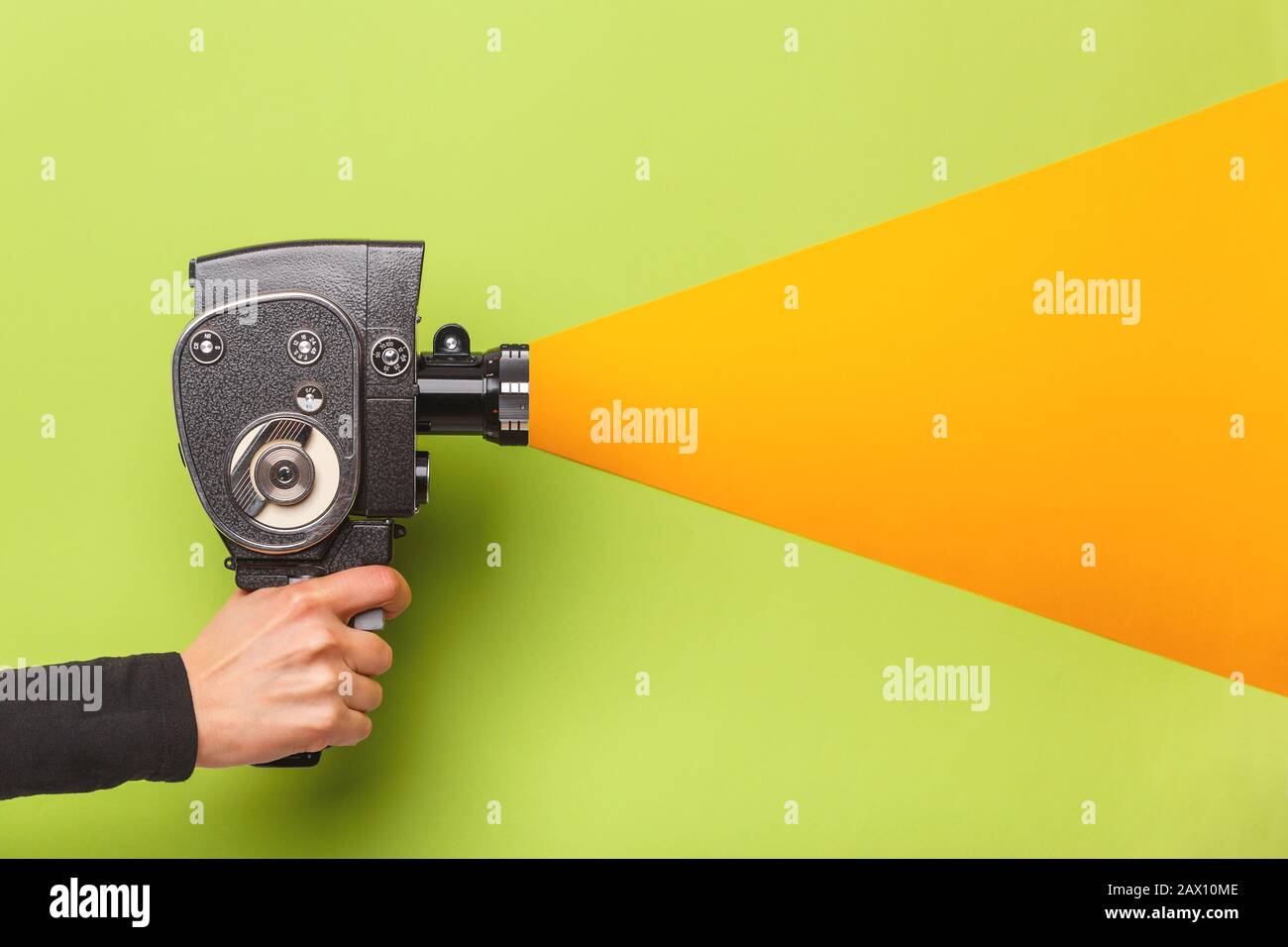 Weibliche Hand, die die Filmkamera im alten Stil imitiert, die den Aufnahmevorgang auf einem grünen Hintergrund mit gelbem Licht durch das Objektiv führt Stockfoto Weibliche Hand, die die Filmkamera im alten Stil imitiert, die den Aufnahmevorgang auf einem grünen Hintergrund mit gelbem Licht durch das Objektiv führt Stockfoto