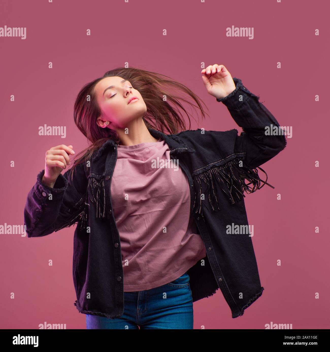 Junge brünette Frau auf pinkfarbenem Hintergrund. Studio-Porträt, informeller Kleidungsstil, Jeans und ein Cowboy-Hemd mit Fransen. Stockfoto