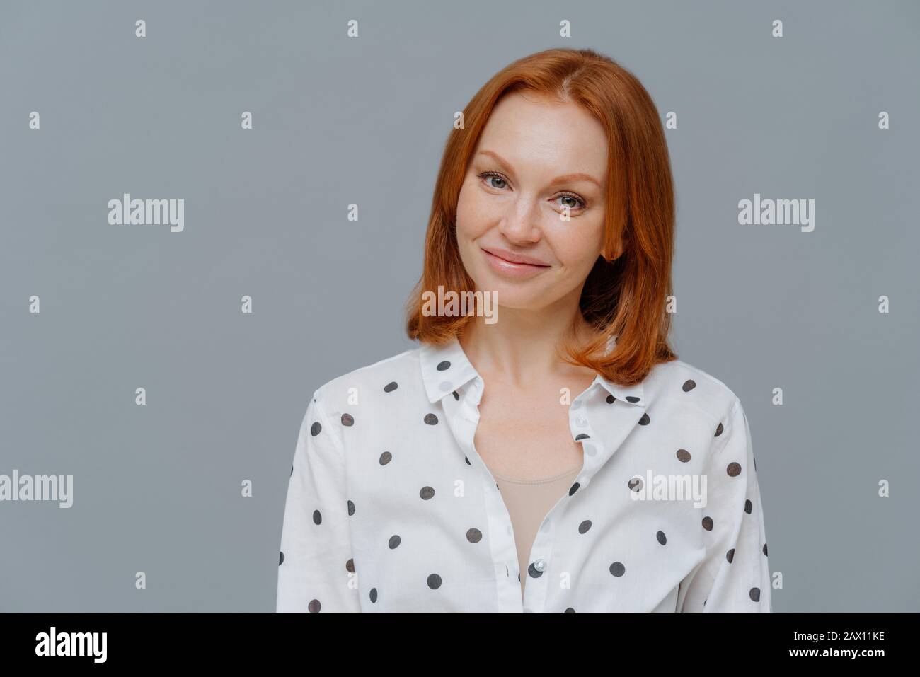 Gefiel Geschäftsfrau mit kurzen roten Haaren, Make-up, sieht positiv auf die Kamera aus, hat nach einem erfolgreichen Geschäftstreffen gute Laune, gekleidet in stilvollem Shi Stockfoto