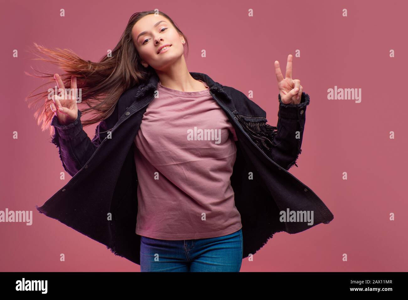 Junge brünette Frau auf pinkfarbenem Hintergrund. Studio-Porträt, informeller Kleidungsstil, Jeans und ein Cowboy-Hemd mit Fransen. Stockfoto