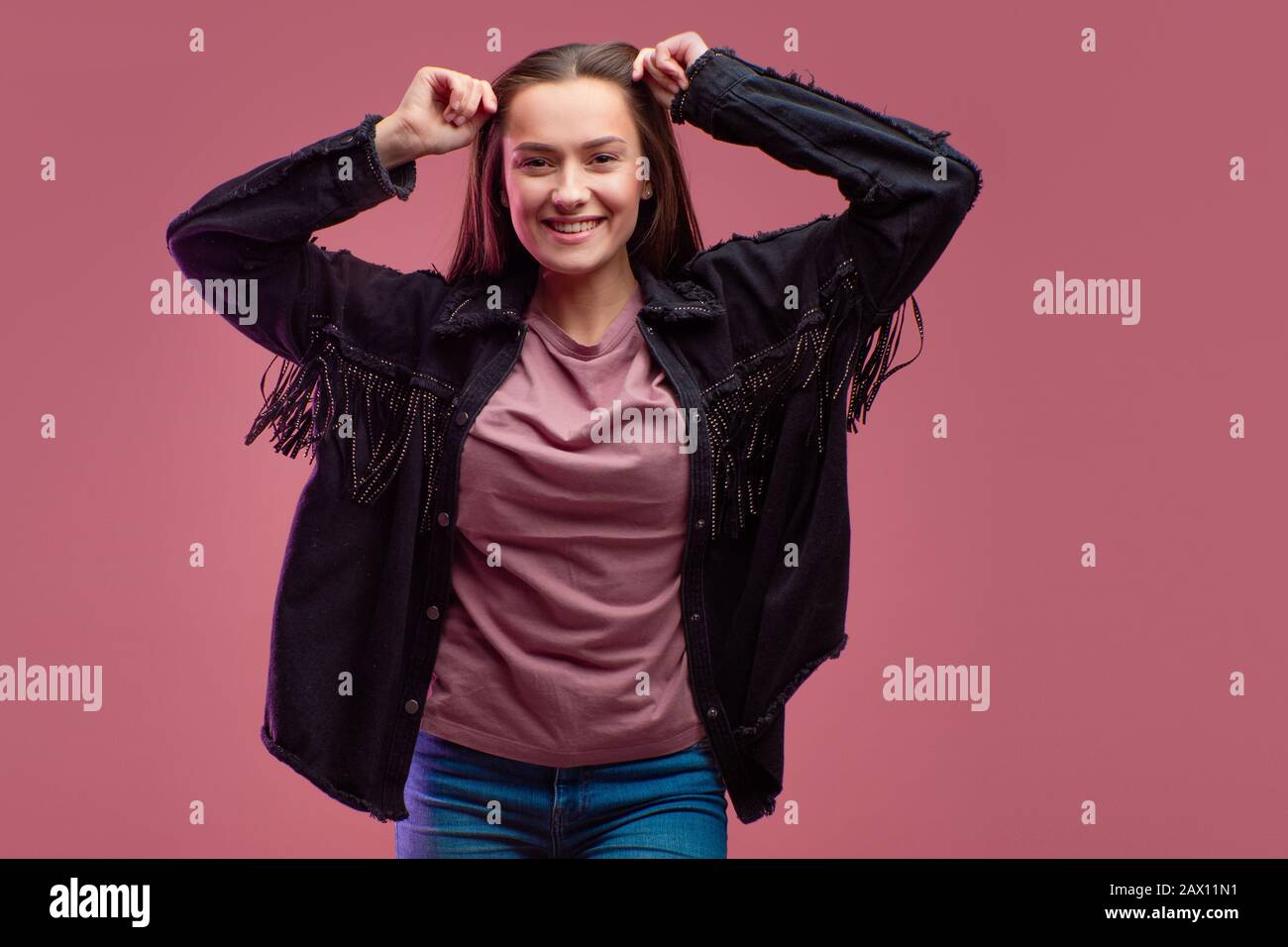 Junge brünette Frau auf pinkfarbenem Hintergrund. Studio-Porträt, informeller Kleidungsstil, Jeans und ein Cowboy-Hemd mit Fransen. Stockfoto