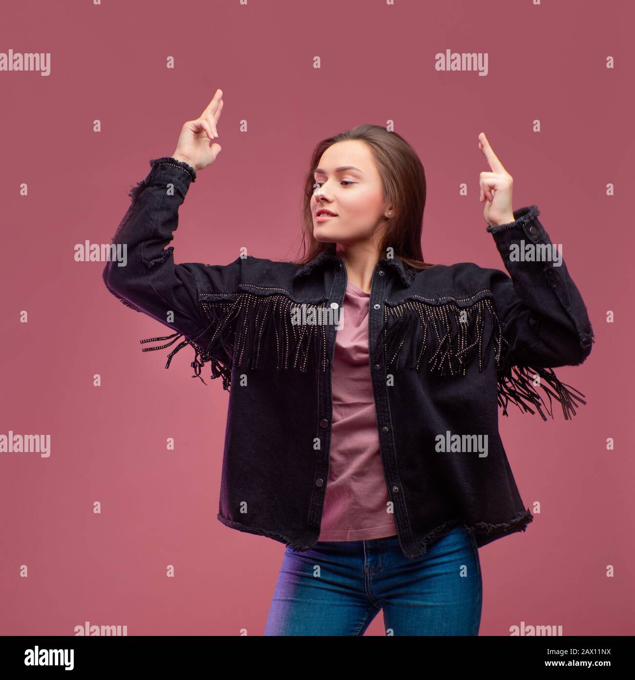 Junge brünette Frau auf pinkfarbenem Hintergrund. Studio-Porträt, informeller Kleidungsstil, Jeans und ein Cowboy-Hemd mit Fransen. Stockfoto