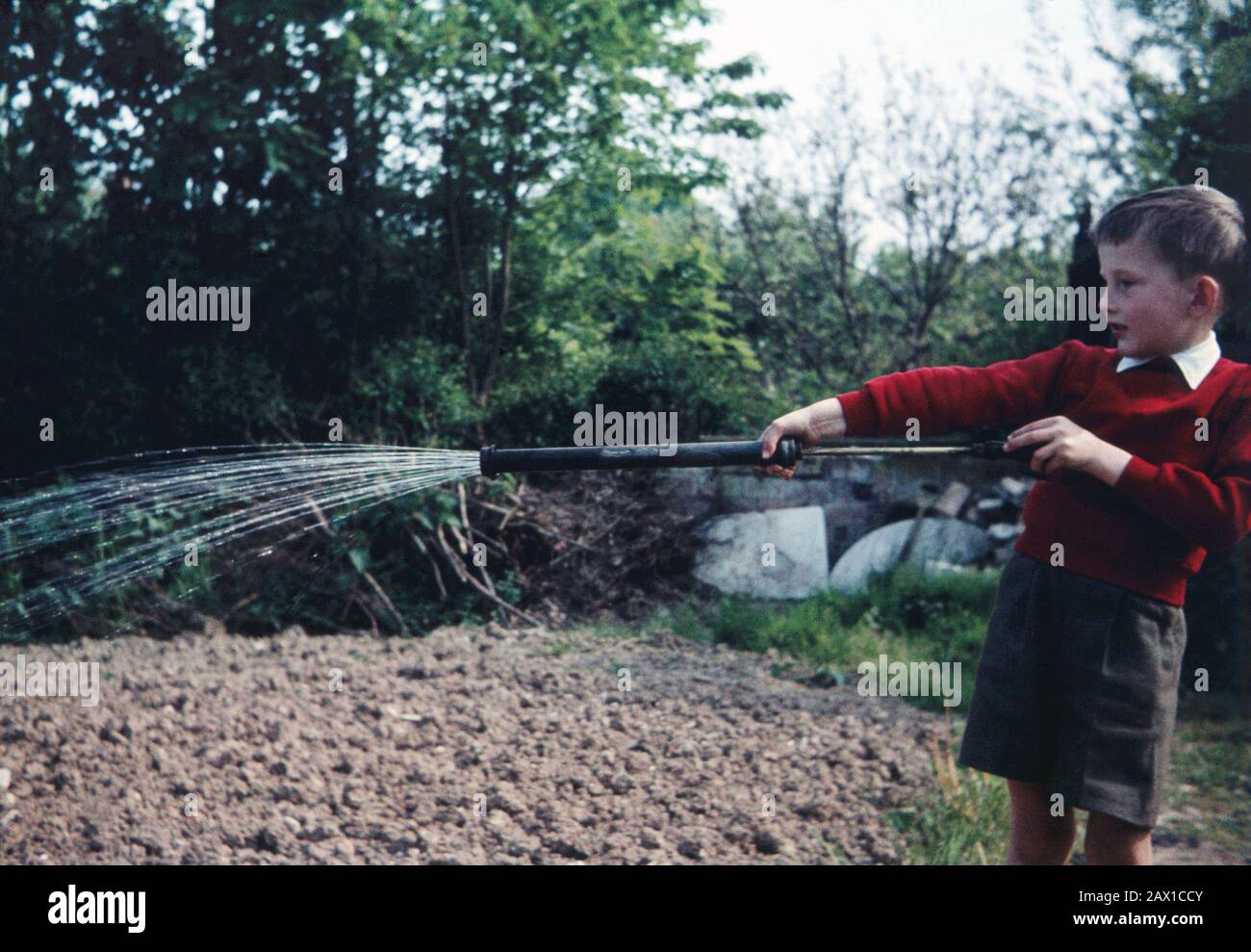 Fünf Jahre alter Junge, der 1959 eine Gartenspritze zum Wassergarten verwendet. Stockfoto