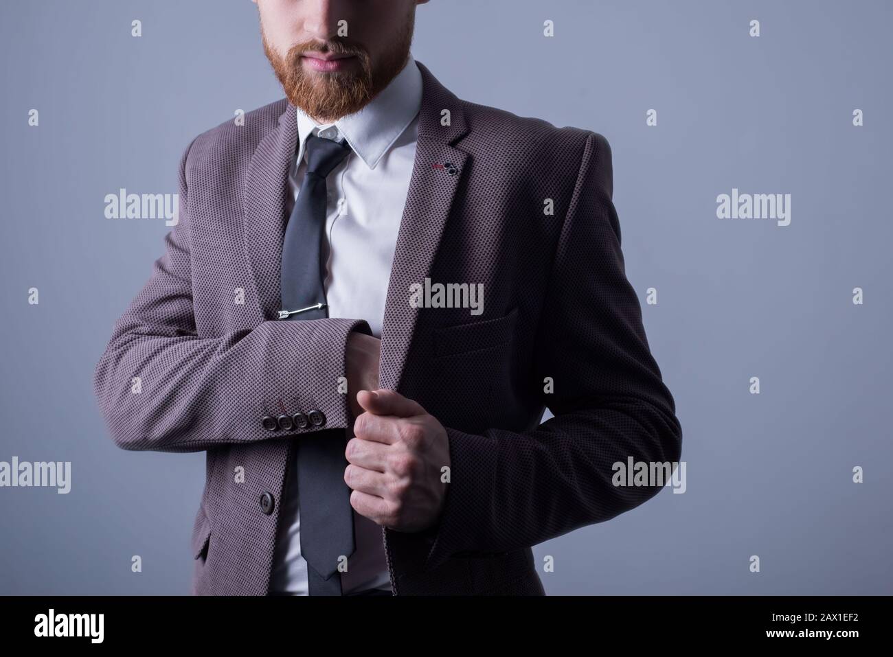 Studio-Porträt eines jungen bärtigen gutaussehenden Kerls von fünfundzwanzig Jahren, in einem offiziellen Anzug, klebt seine Hand in der Innentasche seiner Jacke. Auf Stockfoto