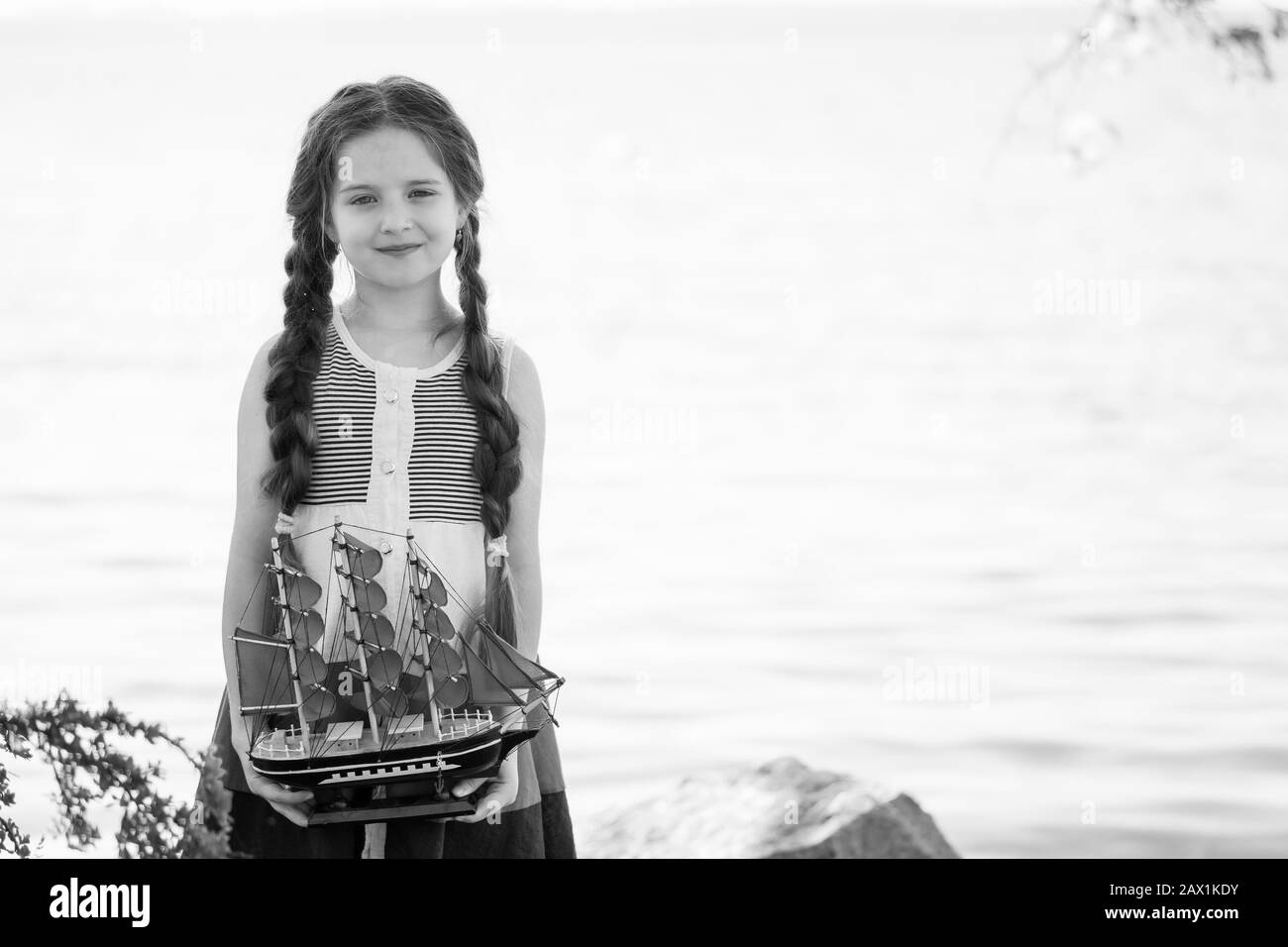 Porträt eines glücklichen kleinen Mädchens am See. In ihren Händen hält sie ein spielzeug-segelboot. Schwarz und Weiß. Stockfoto