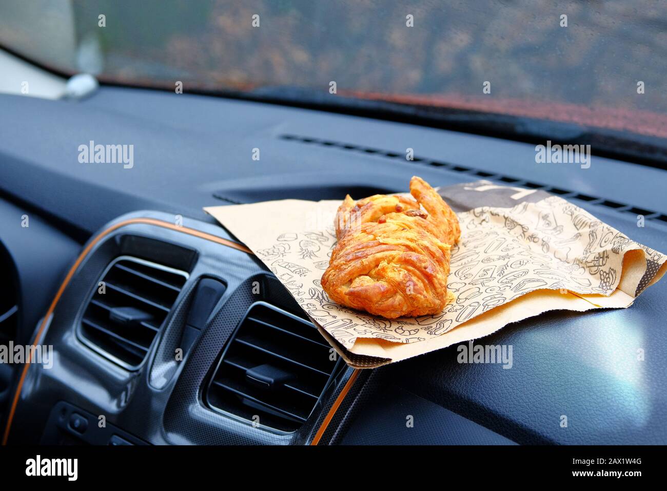 Gedrehter zuckerhaltiger Bun zum Mittagessen. Süßer Snack auf der Konsole im Auto. Mittagspause während der Fahrt mit dem Auto. Mitnahme, soziale Medien. Stockfoto