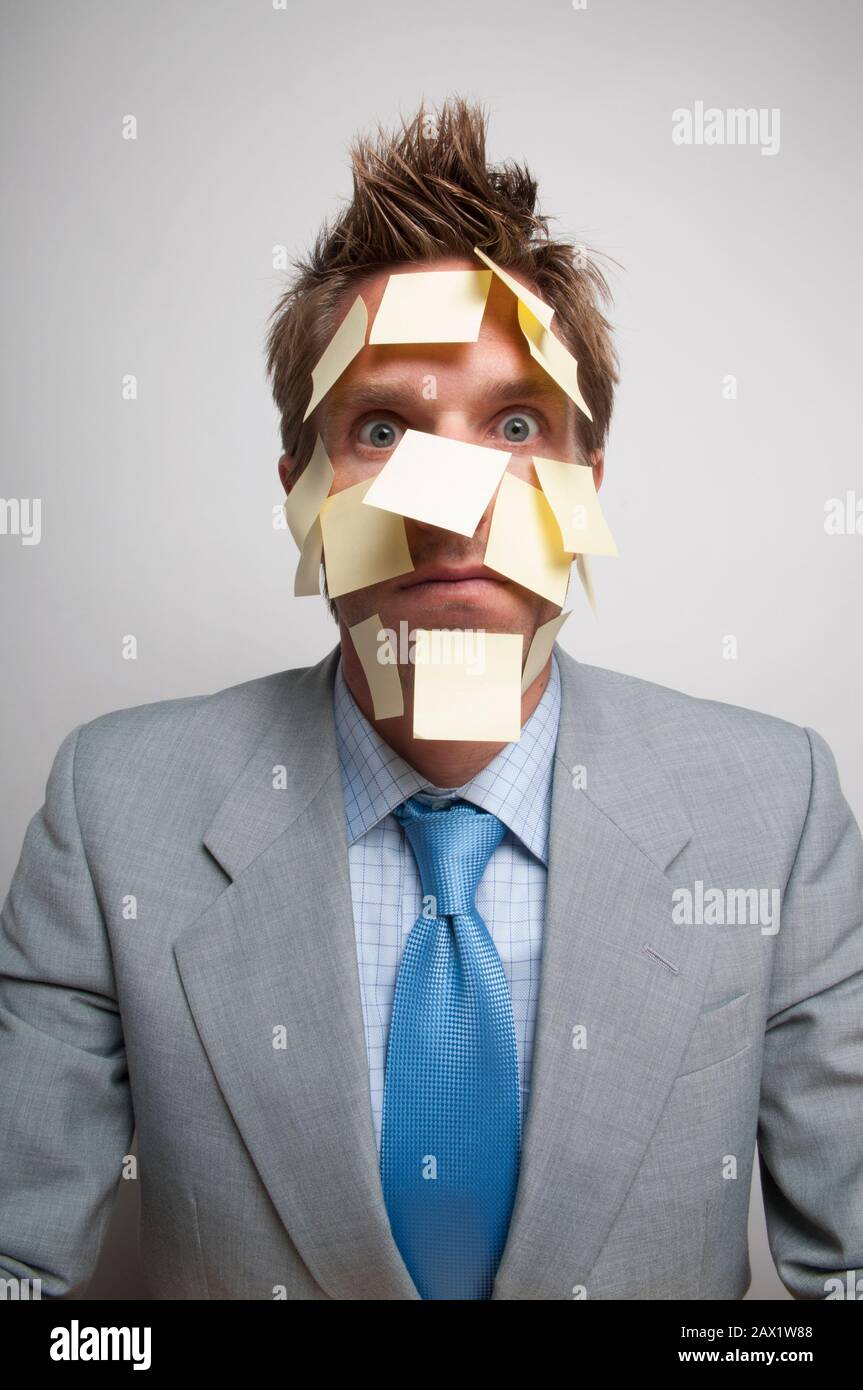 Erschöpfter Büroangestellter, der die Kamera mit gelben Haftnotizen im ganzen Gesicht betrachtet Stockfoto