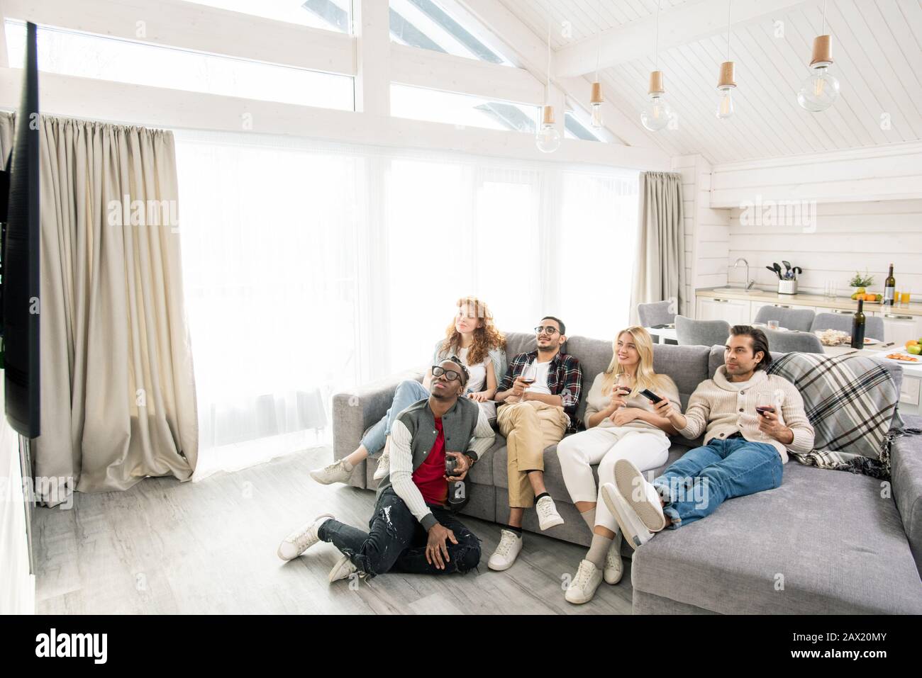 Junge Männer und Frauen sitzen entspannt auf dem Sofa in modernen Apartments und sehen Filme im Fernsehen, horizontaler Hochwinkel Stockfoto