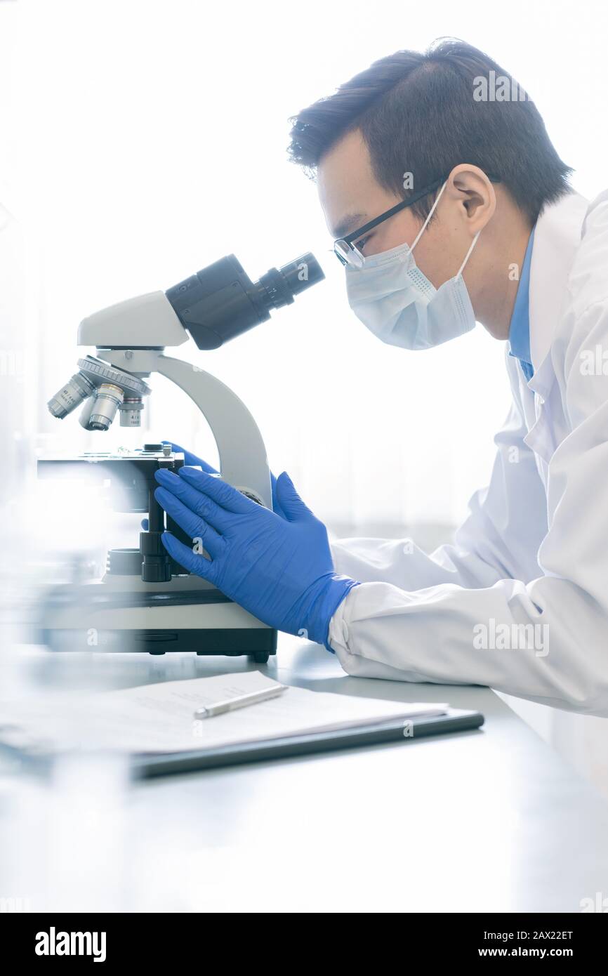 Vertikales Seitenbild des jungen männlichen Pharmakologen, der die chemische Reaktion der Proben mit dem Mikroskop in modernen Labors untersucht Stockfoto