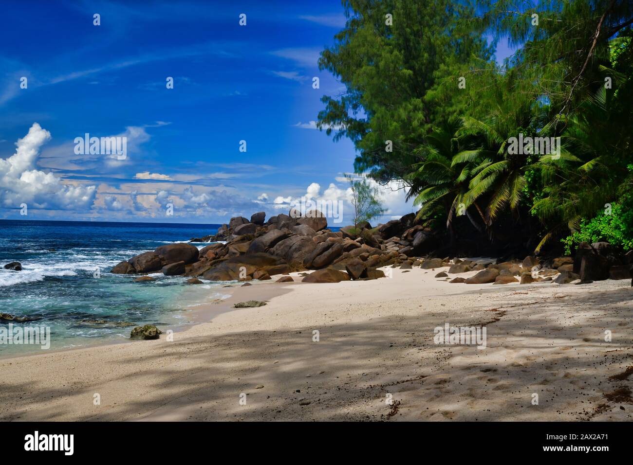 Meereswellen und Granit-Felsen Takamaka Beach, Mahe Island, Seychellen. Palmbäume, Sand, abstürmende Wellen, schönes Ufer, blauer Himmel und türkisfarbenes Wasser Stockfoto