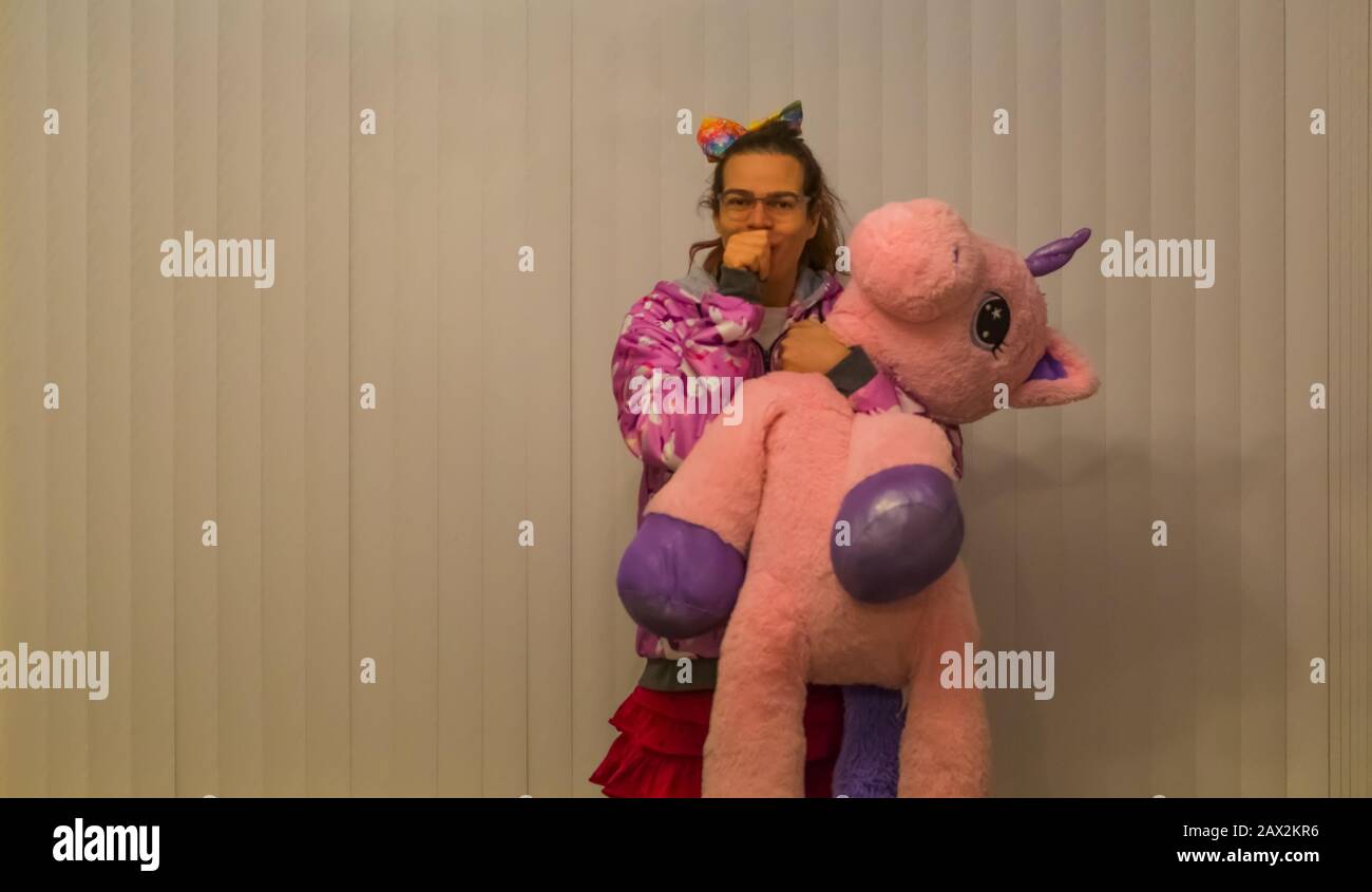 Porträt eines lustigen und süßen Transgender-Mädchens, das ein gestopftes, rosafarbenes Einhorn hält und ihren Daumen saugt, Infantiles Verhalten bei Erwachsenen, LGBT Diversity, Autism a Stockfoto
