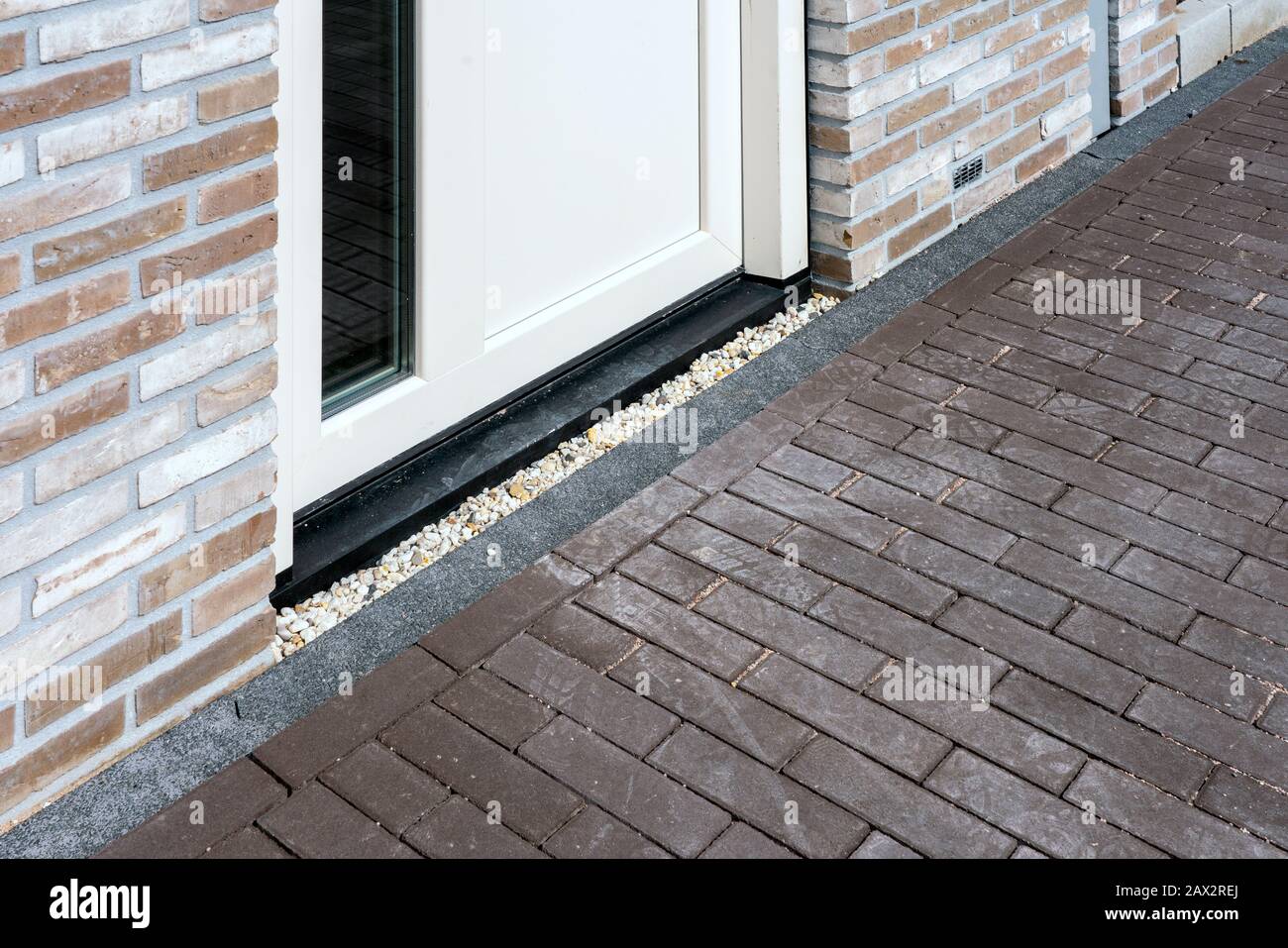 Nahaufnahme der weißen modernen Tür mit Ziegelfassade und Kopfsteinpflaster am Fußweg. Stockfoto