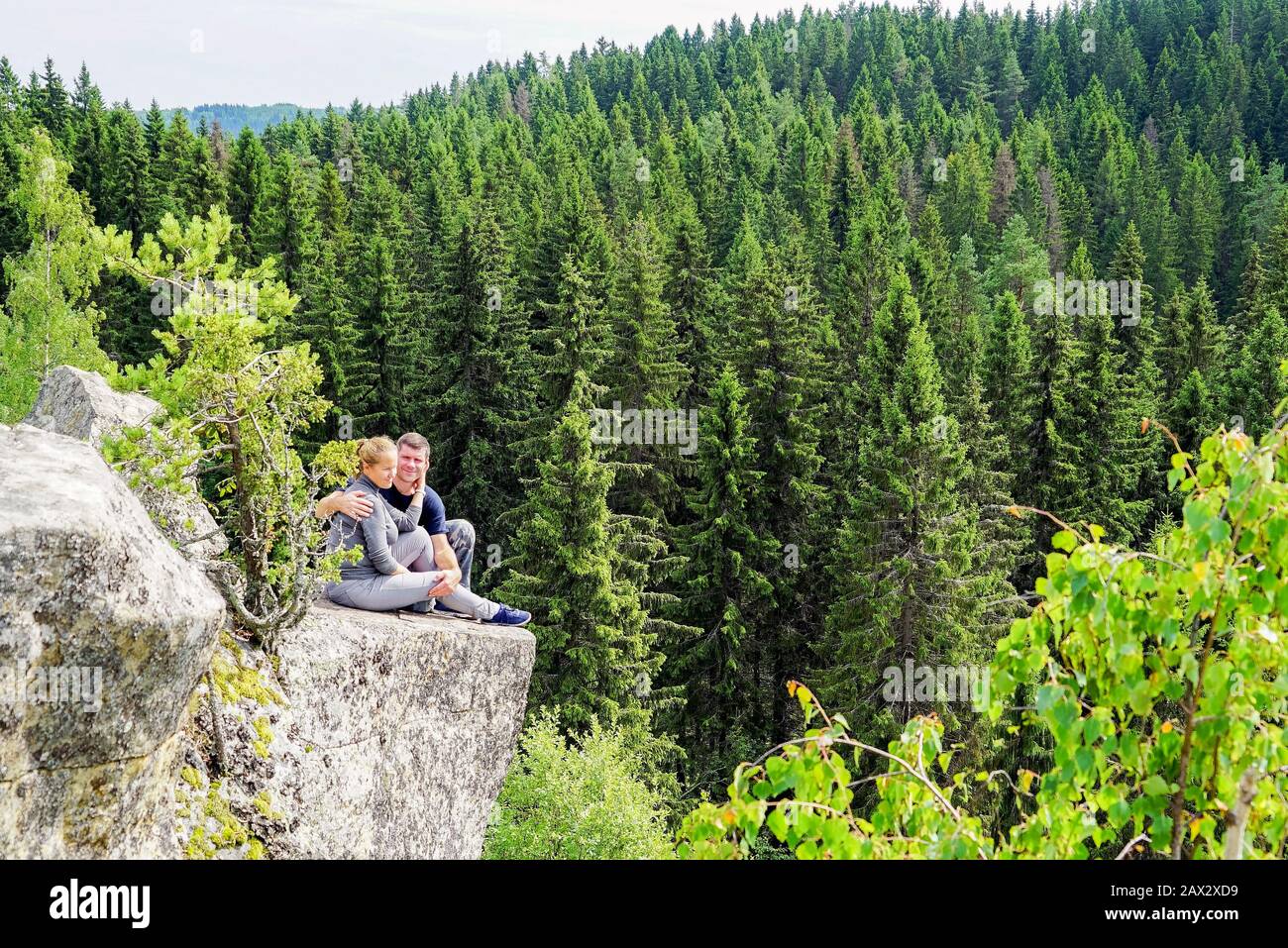Ein Mann und eine Frau sitzen umarmend am Rande eines Berges in der Natur Stockfoto