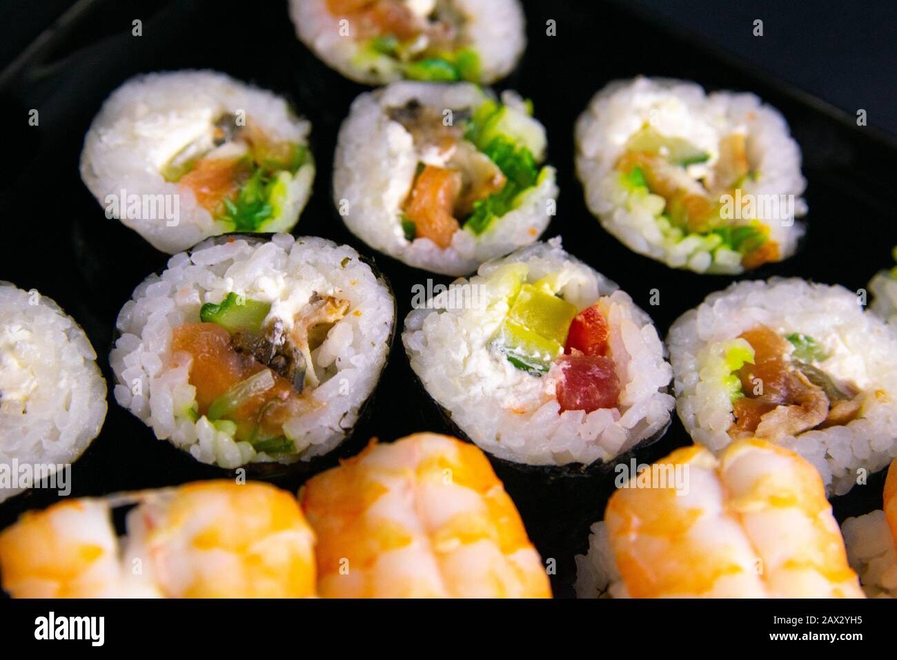 Brötchen und Mohn liegen in der Nähe von Lachs, Garnelen, Avocado, Gurken und Algen. Stockfoto