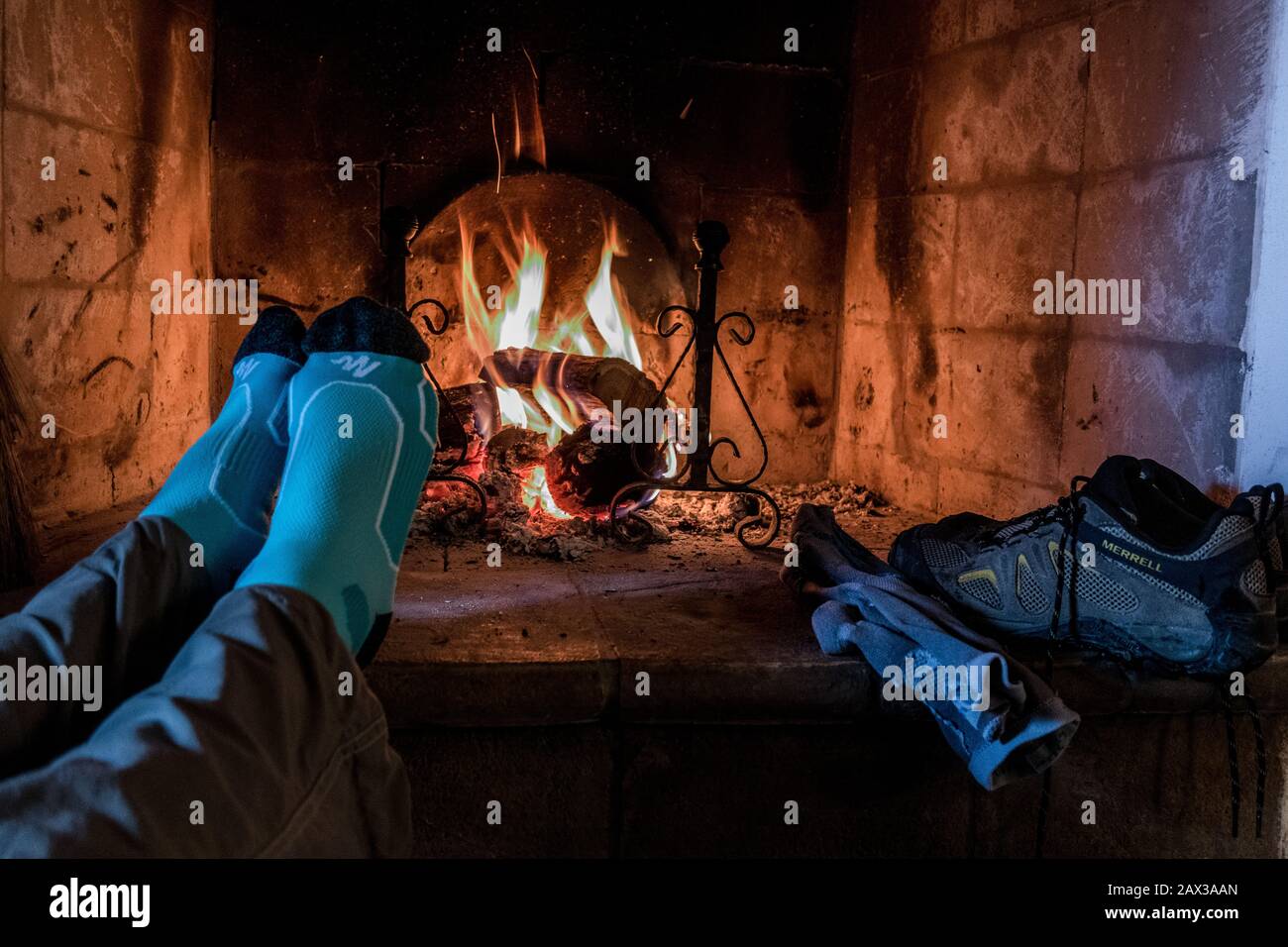 Socken Wanderschuhe und Füße warnen vor einem glühenden offenen Holzfeuer Stockfoto