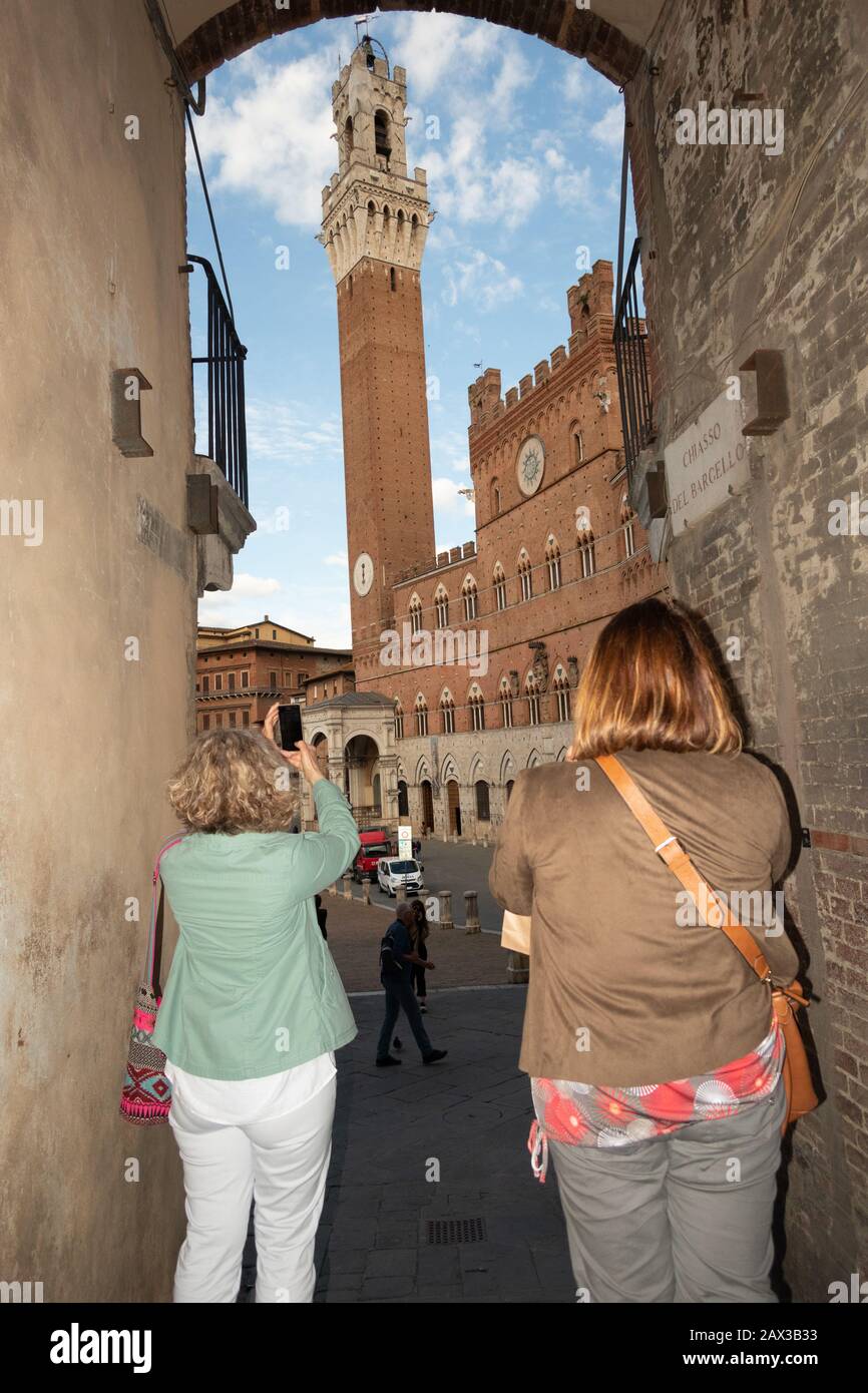 Touristen fotografieren im Bogen den Turm von Mangia auf der Piazza del Campo von icolo del Bargello in Siena Toskana Italien Stockfoto