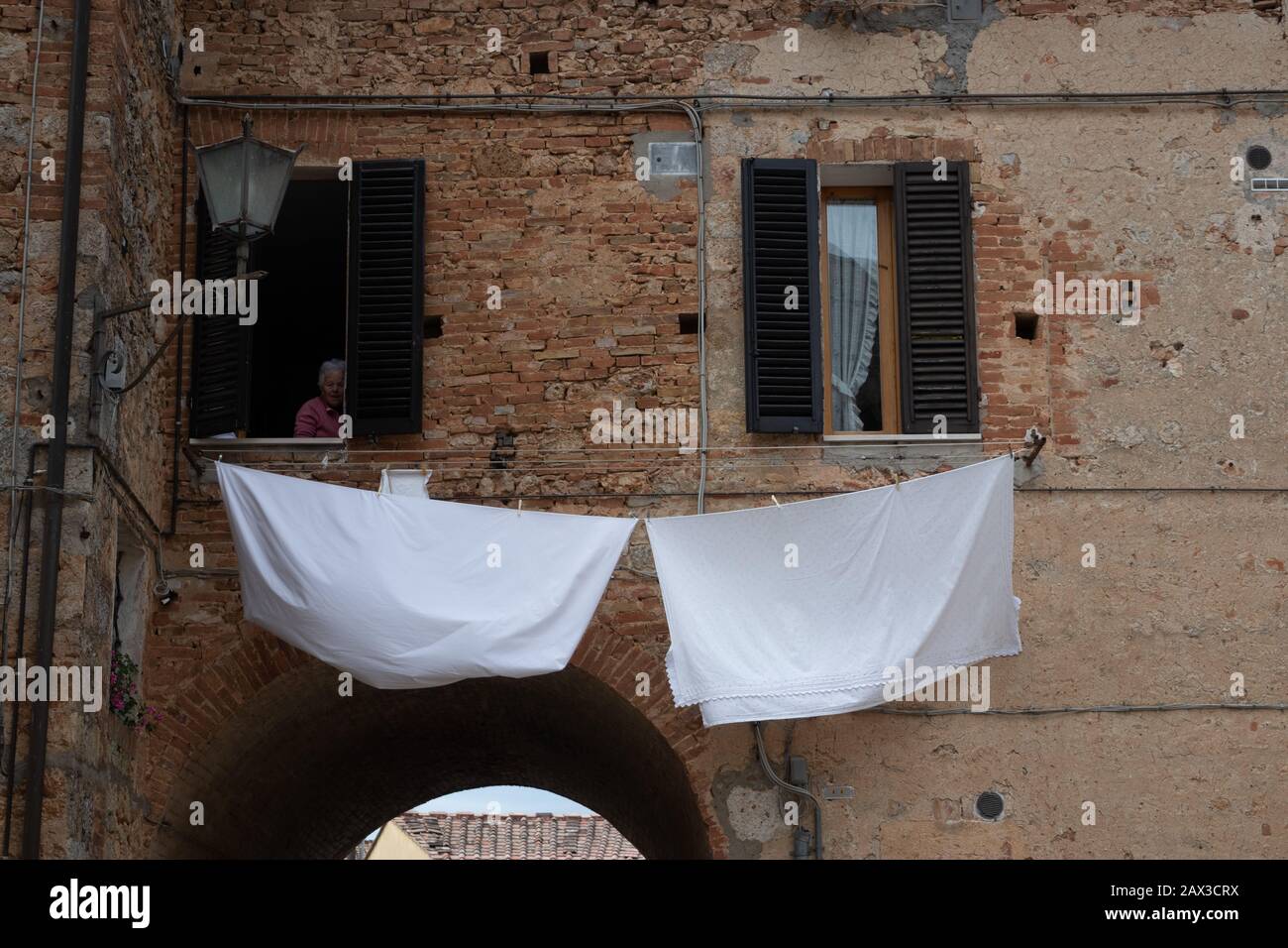Frau, die aus dem Fenster blickt und die Luft trocknet, die unten in Monteriggioni, einem mittelalterlichen, ummauerten, befestigten Weiler, der Toskana, Italien, trocknet Stockfoto