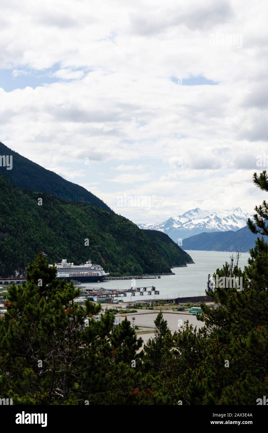 Bild auf einem Hügel des Skagway-Ports mit dem Kreuzfahrtschiff der Holland America Line am Hafen. Berge im Hintergrund und übergiebelten Tag. Stockfoto