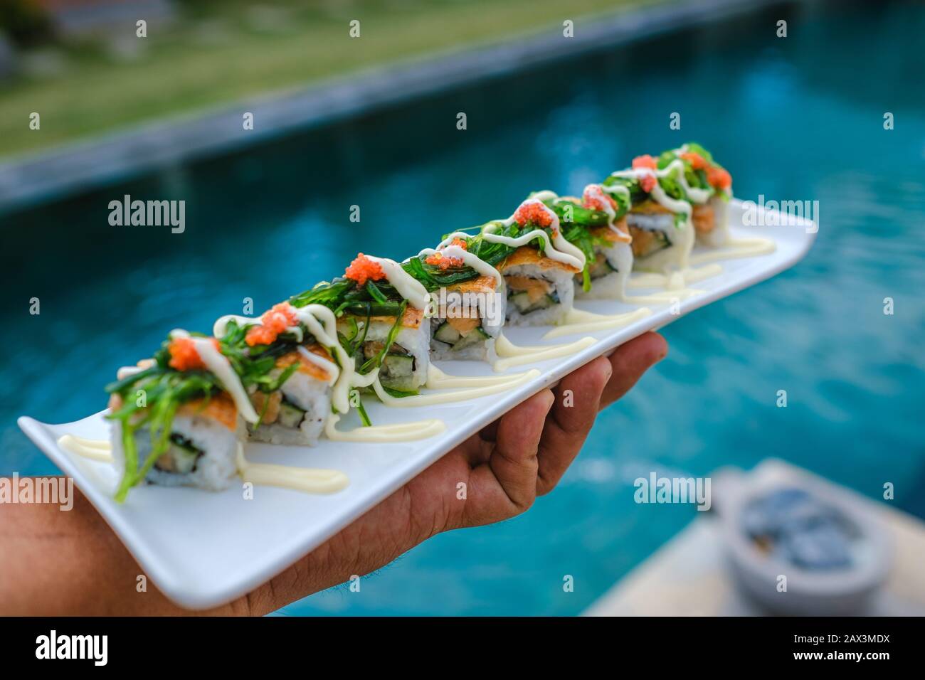 Halten Sie ein Tablett mit Sushi vor dem Pool Stockfoto