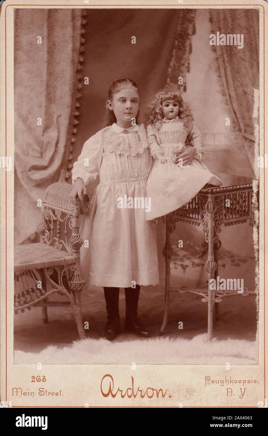 1900 Ca, New Yersey, USA: Kleine Mädchen mit Puppe. Foto von Ardron , Poughkeepsie , NEW YERSEY - FOTO STORICHE - HISTORIENFOTOS - BAMBINA - KIND - BAMBINO - BAMBINI - BAMBINE - KINDER - ZÄRTLICH - KINDER - BAMBINA - BABY - BELLE EPOQUE - MODE - MODA-INFANTILE - BABY - BEBÉ - ROSA KLEID - KINDHEIT - INNZIA - Bambola - Bambole - Spielzeuge - Giocattolo - giocattoli - gioco - Spiel - poltrona di vimini - Rattan - pizzo - Spitze ---- Archivio GBB Stockfoto